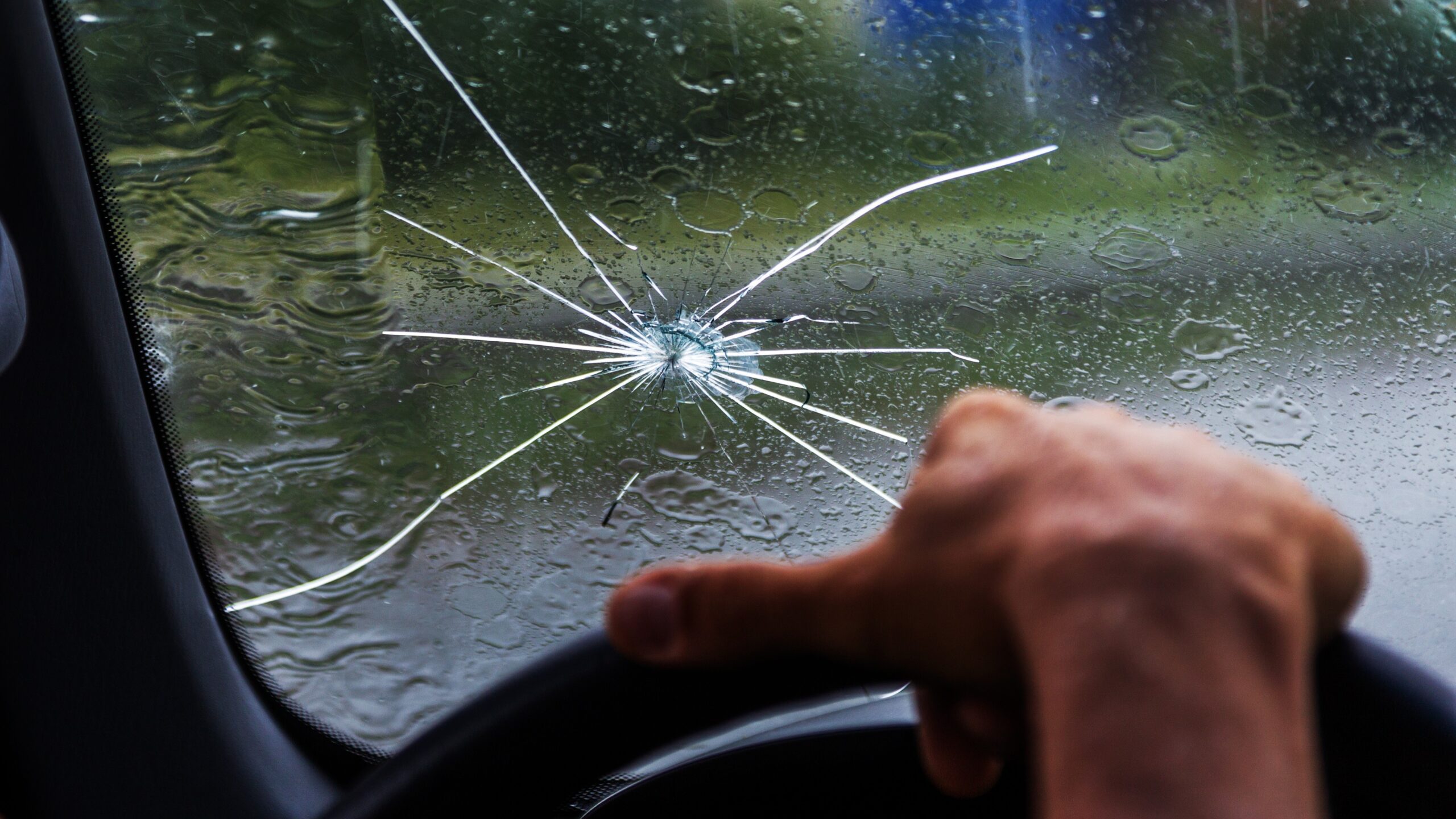 Cracked windshield with man's hand on steering wheel 